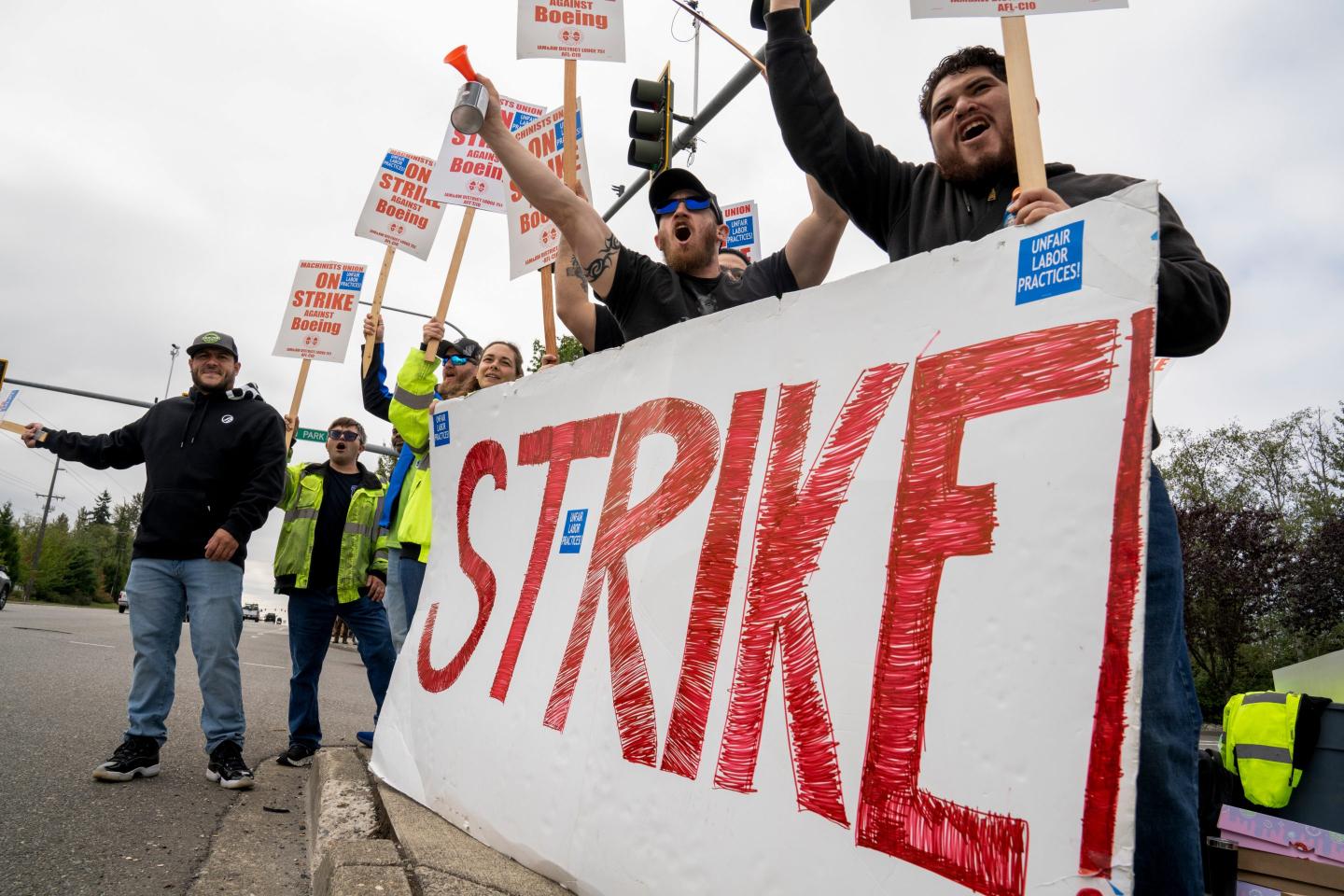 Boeing workers hold out a sign that says "Strike" in big red letters, as well as other smaller signs.