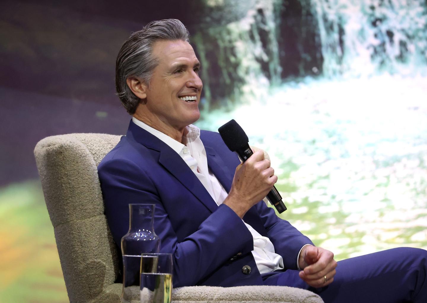 Governor newsom smiles holding a microphone on stage
