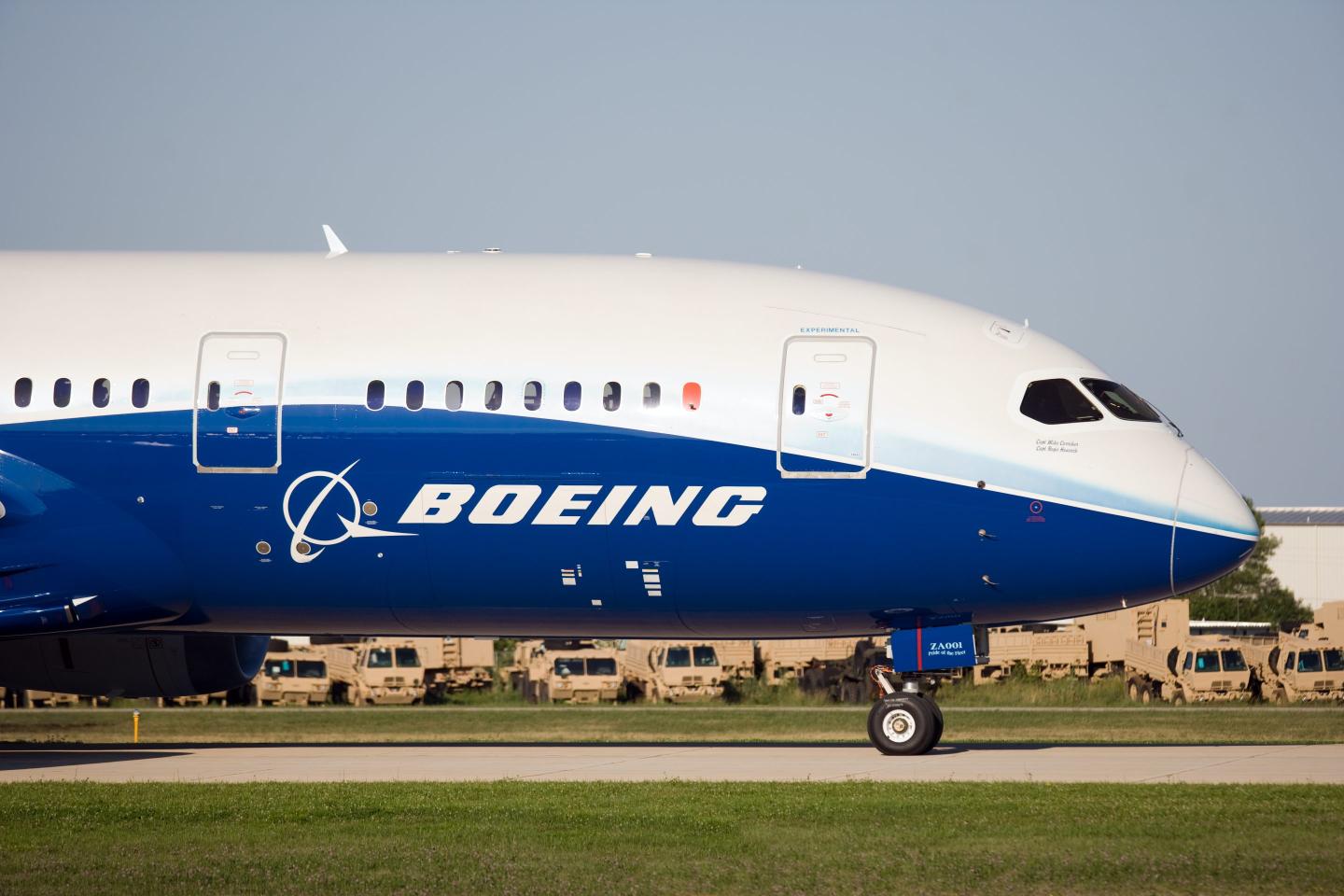 A boeing plane, logo clearly displayed, sits on a tarmac. The plane is half white and half Boeing's signature blue.