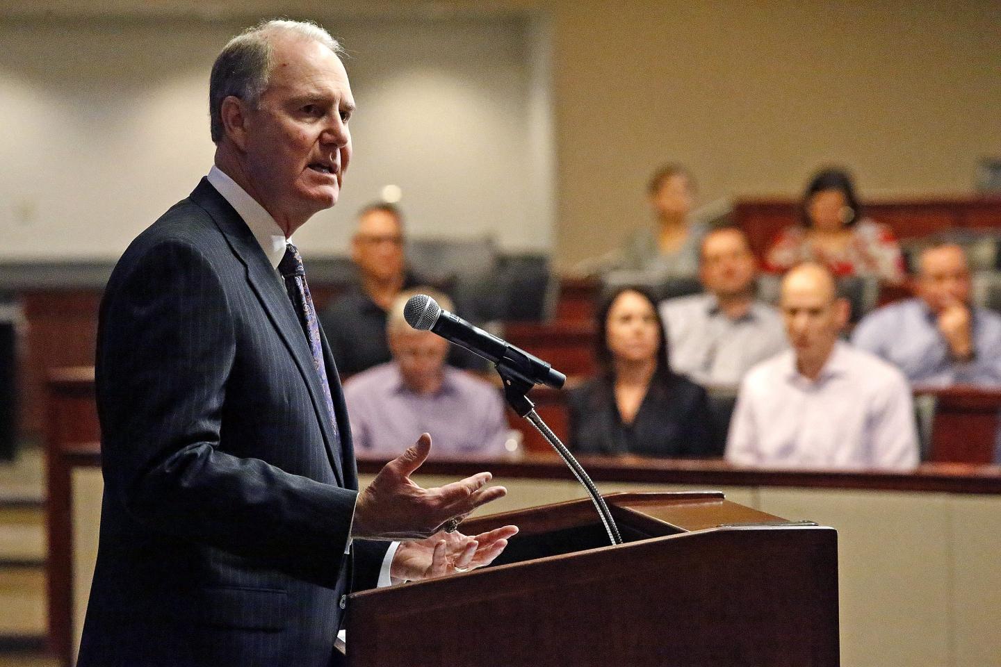 Southwest chairman Gary Kelly grimaces and lifts both hands, palms up, as he speaks at a podium during a press conference.