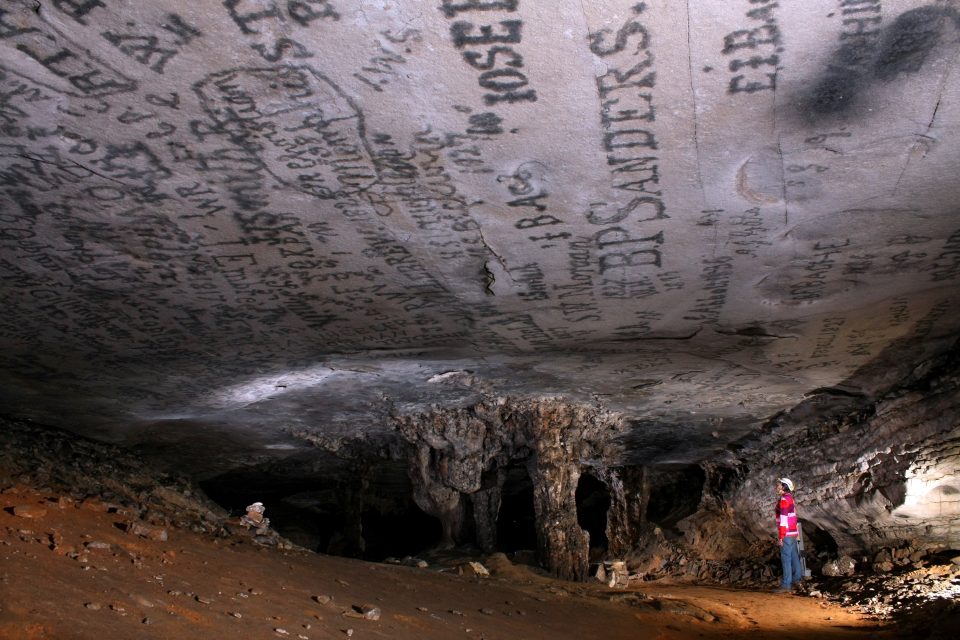 A woman in a cave looks up at the ceiling with words written on it.