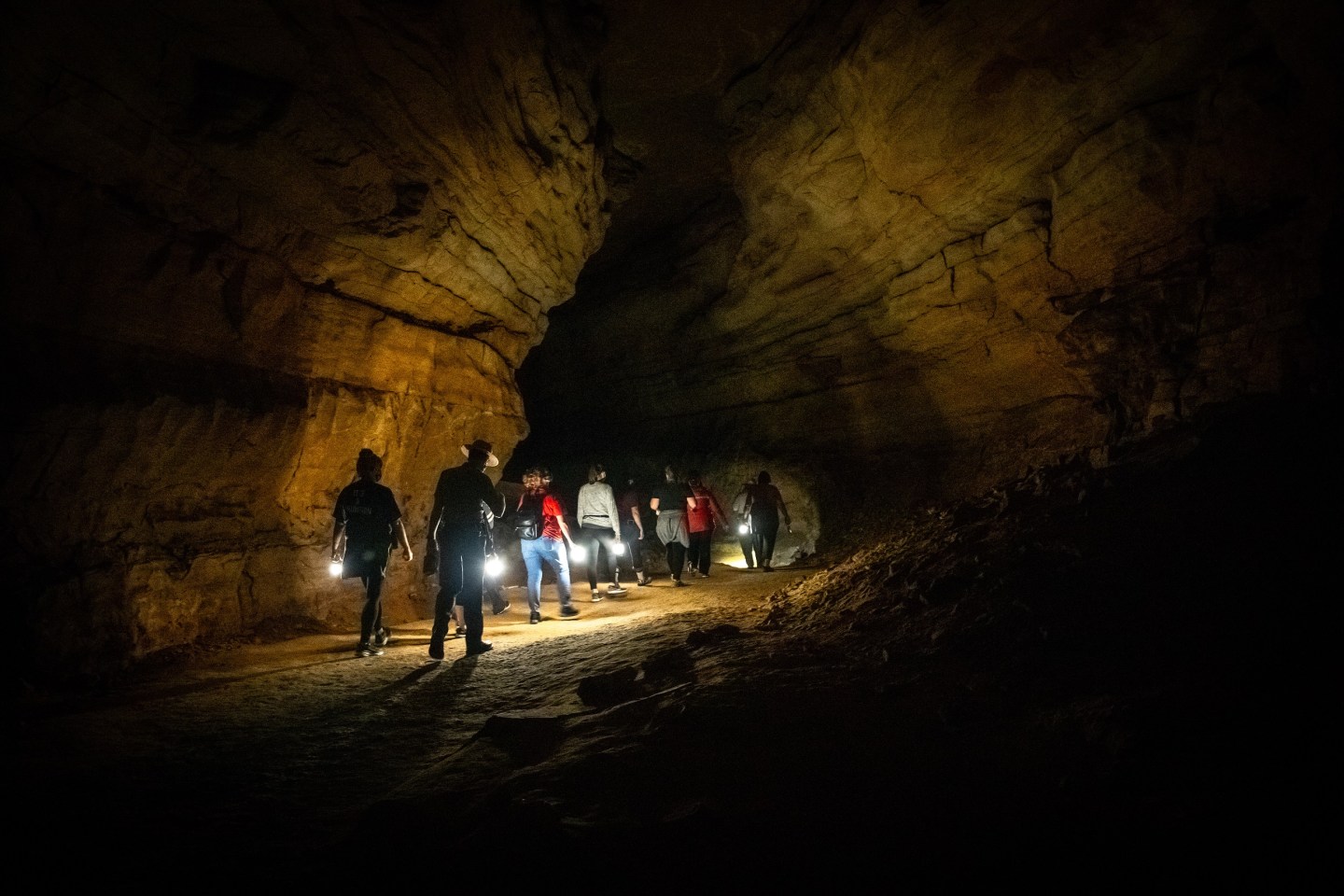 A dark cavern is lit by people holding lanterns.
