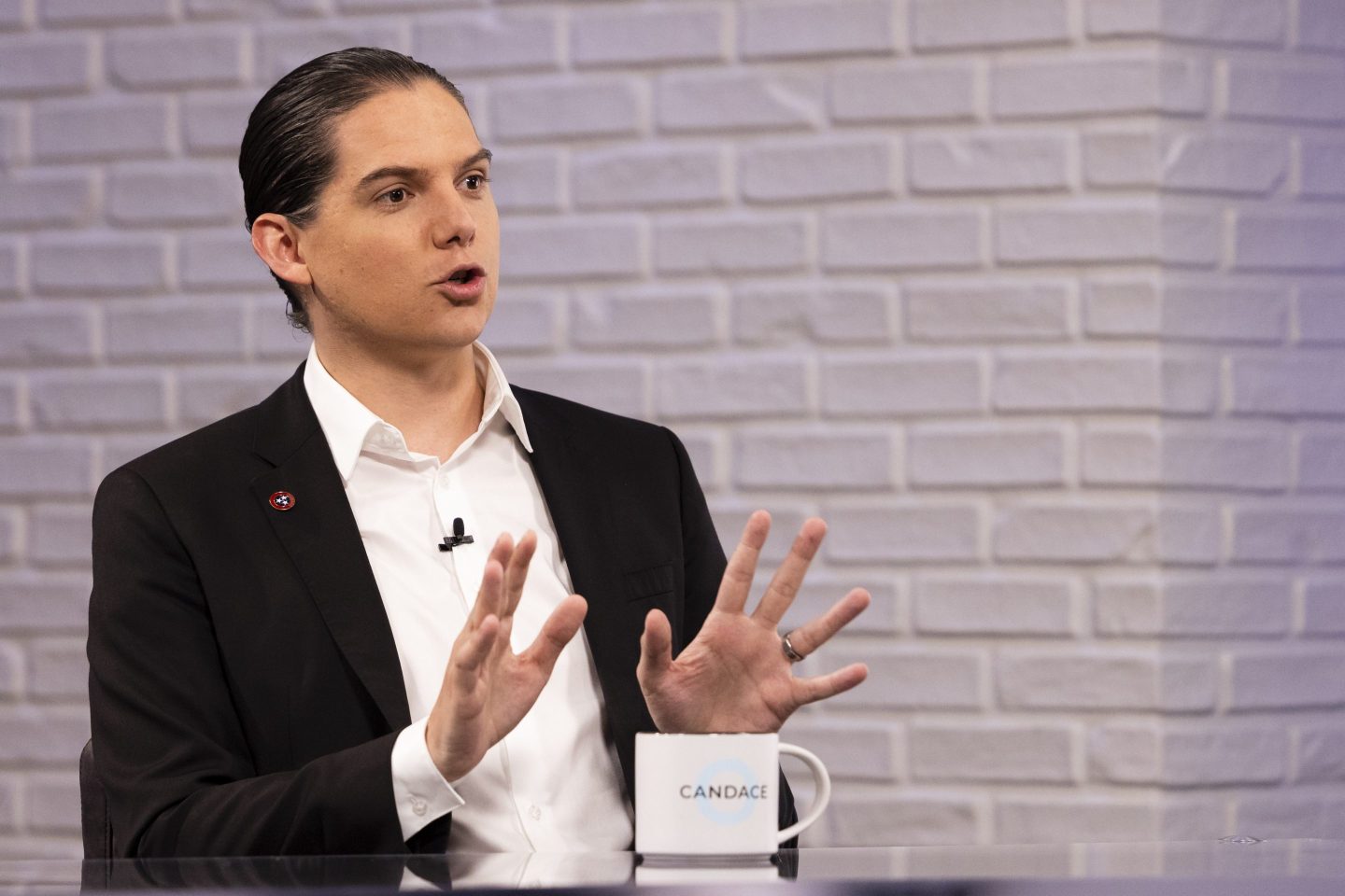 Robby Starbuck sits at a table in. a black jacket and white shirt
