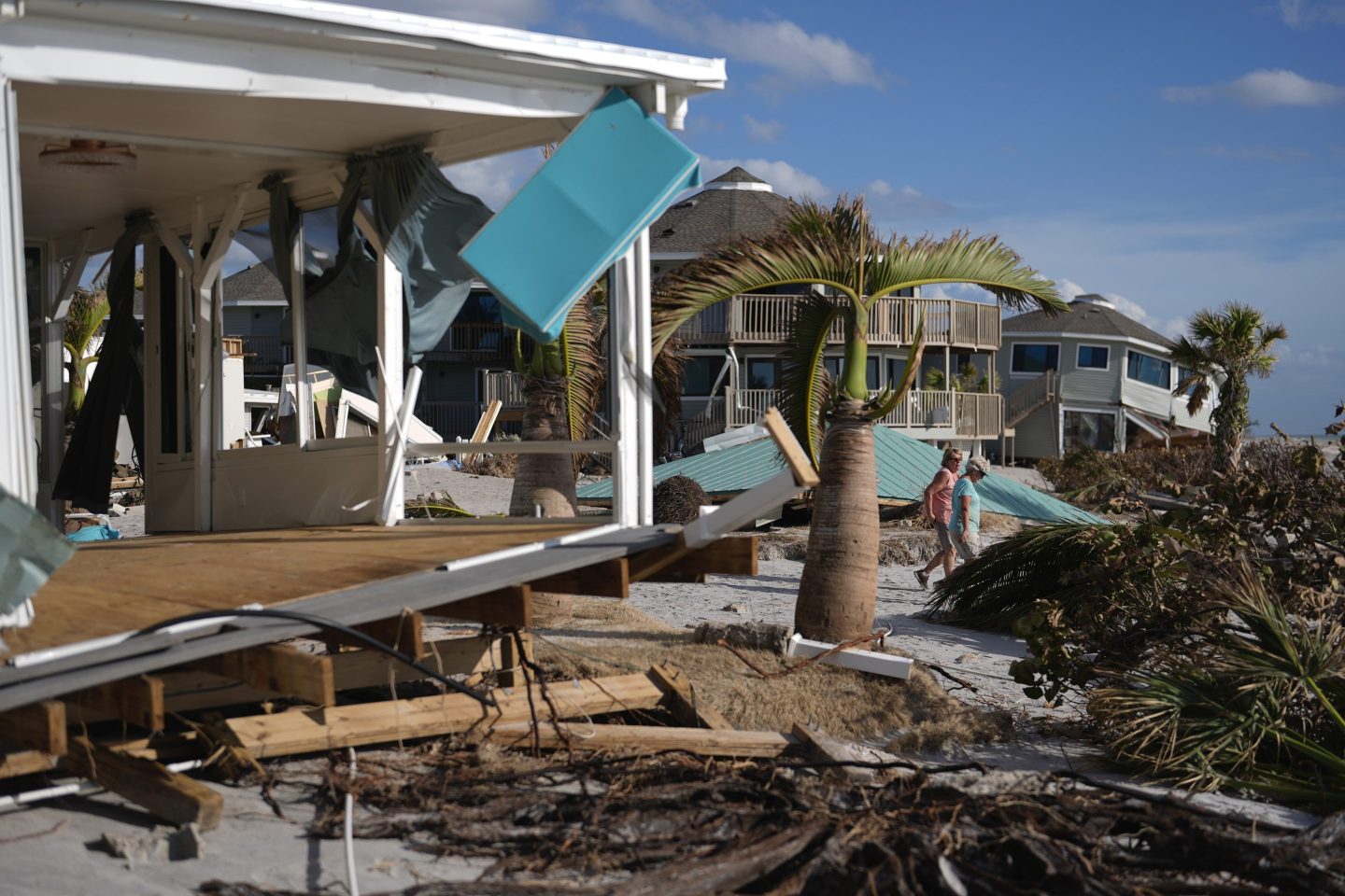 Resident Kerry Flynn, right, and a friend walk past a damaged home and the displaced roof of their 55+ mobile home community's tiki hut after the passage of Hurricane Milton, on Manasota Key, in Englewood, Fla., Oct. 13, 2024.