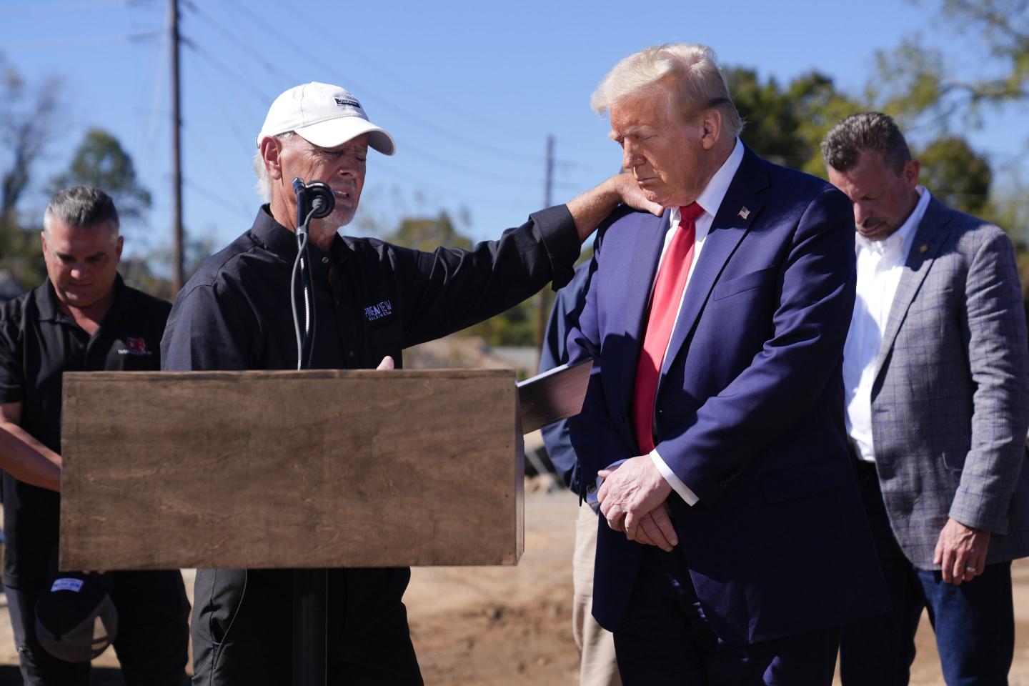 Republican presidential nominee former President Donald Trump prays with Mike Stewart, owner of Pine View Buildings, and others, after delivering remarks on the damage and federal response to Hurricane Helene.
