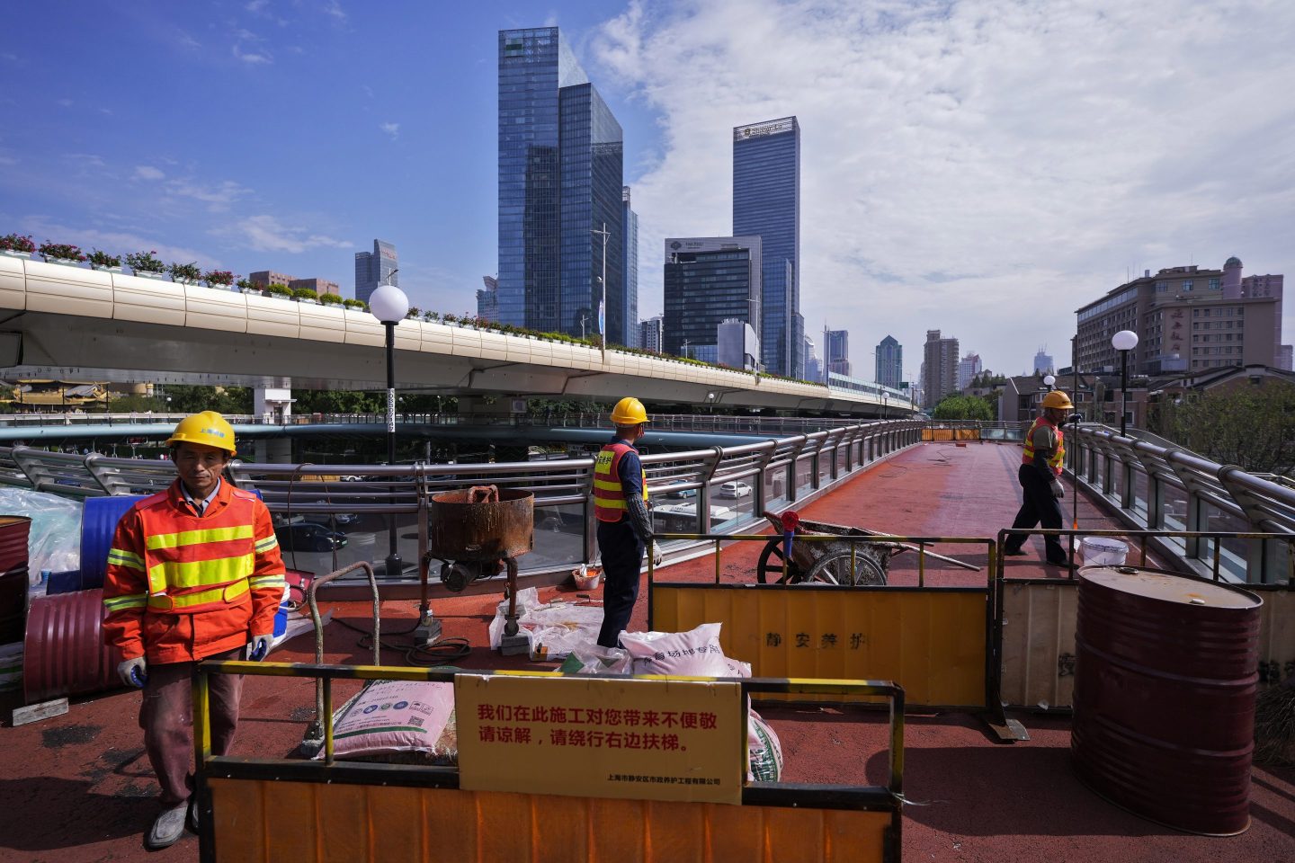 The city of Shanghai is seen in the background as construction workers refurbish an overhead pedestrian bridge.