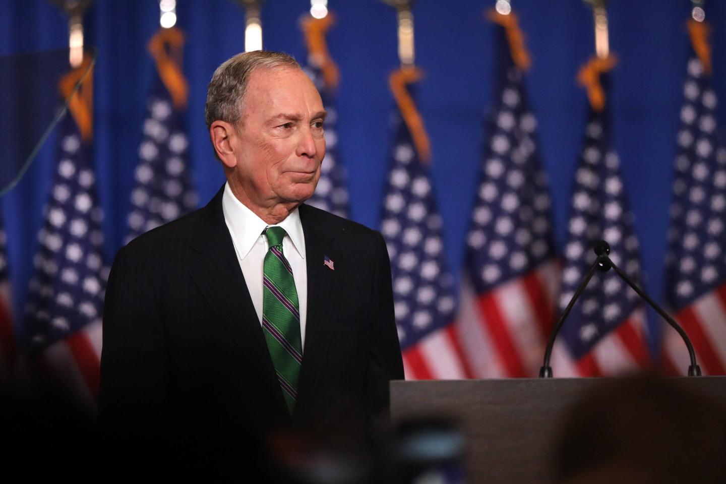 Mike Bloomberg standing in front of American flags