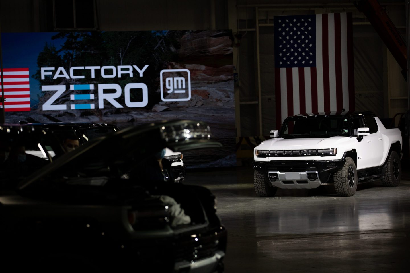 A GMC Hummer electric vehicle is seen surrounded by other vehicles with partial view of GM's Factory Zero logo in the background.