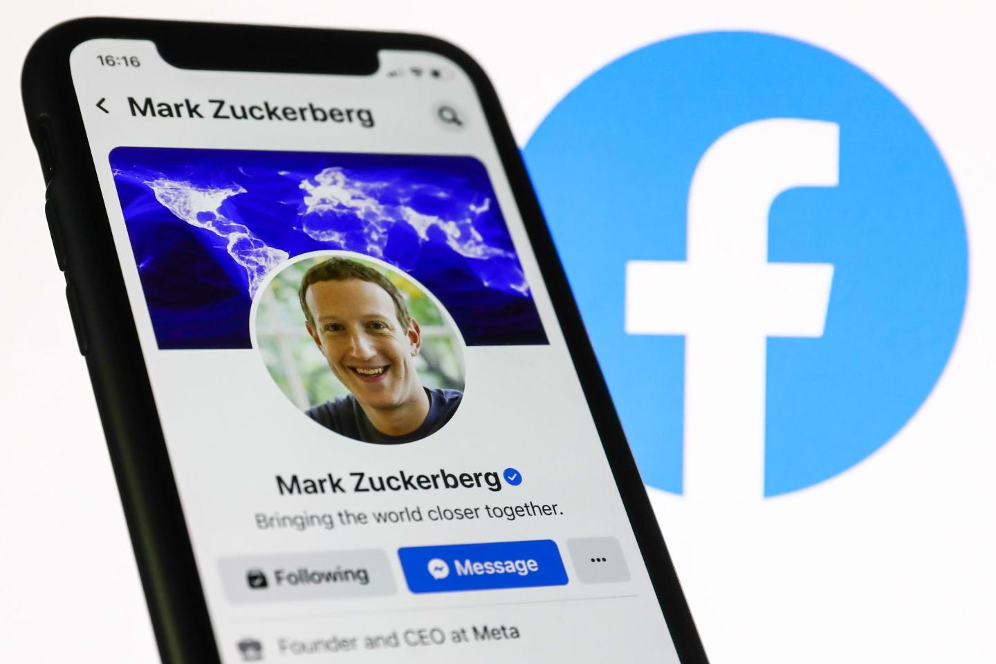 Mark Zuckerberg's Facebook profile displayed on a phone screen and Facebook logo displayed on a screen in the background are seen in this illustration photo.