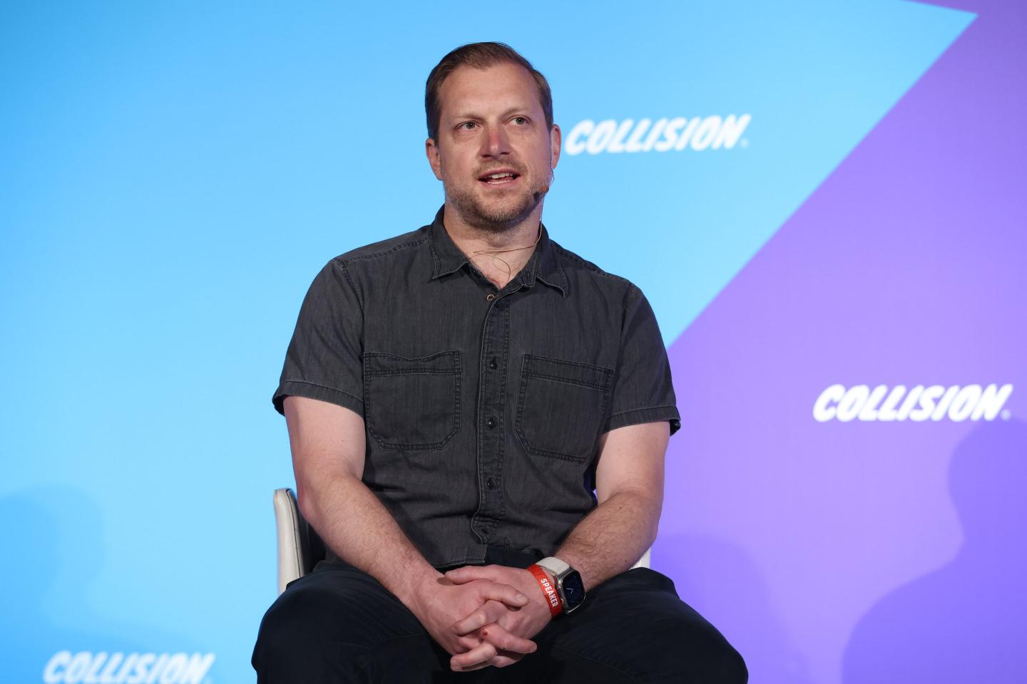 A man in a button down t-shirt sits on stage