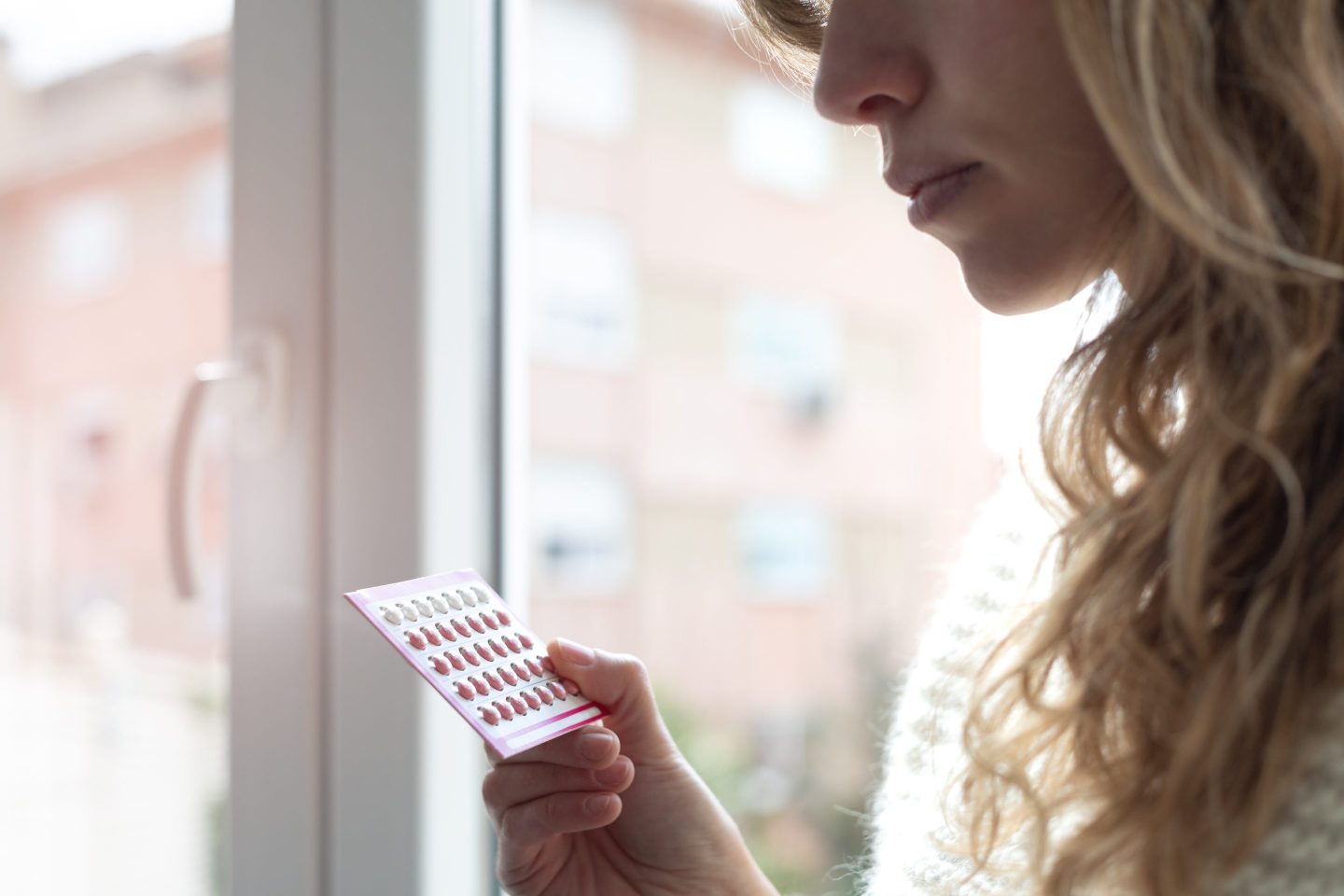 oral contraceptives in the hand of a woman whose face is partially visible in the top right corner of the frame