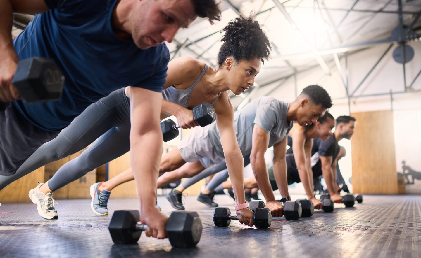 Men and women in a gym class doing planks with their hands on weights