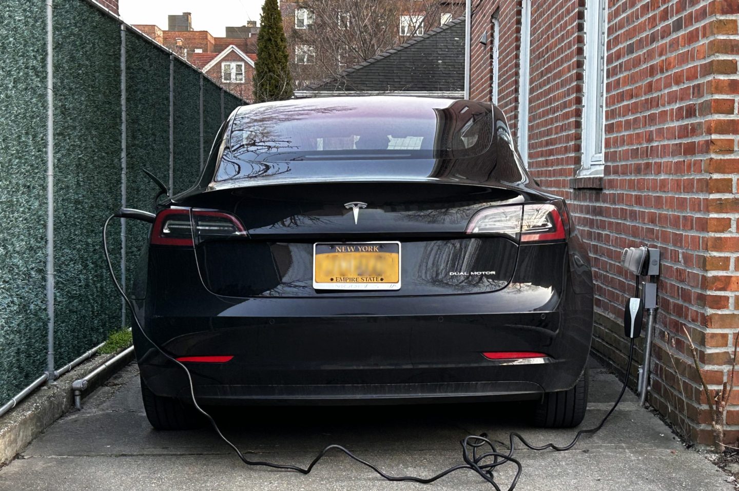 A Tesla car charging next to a house