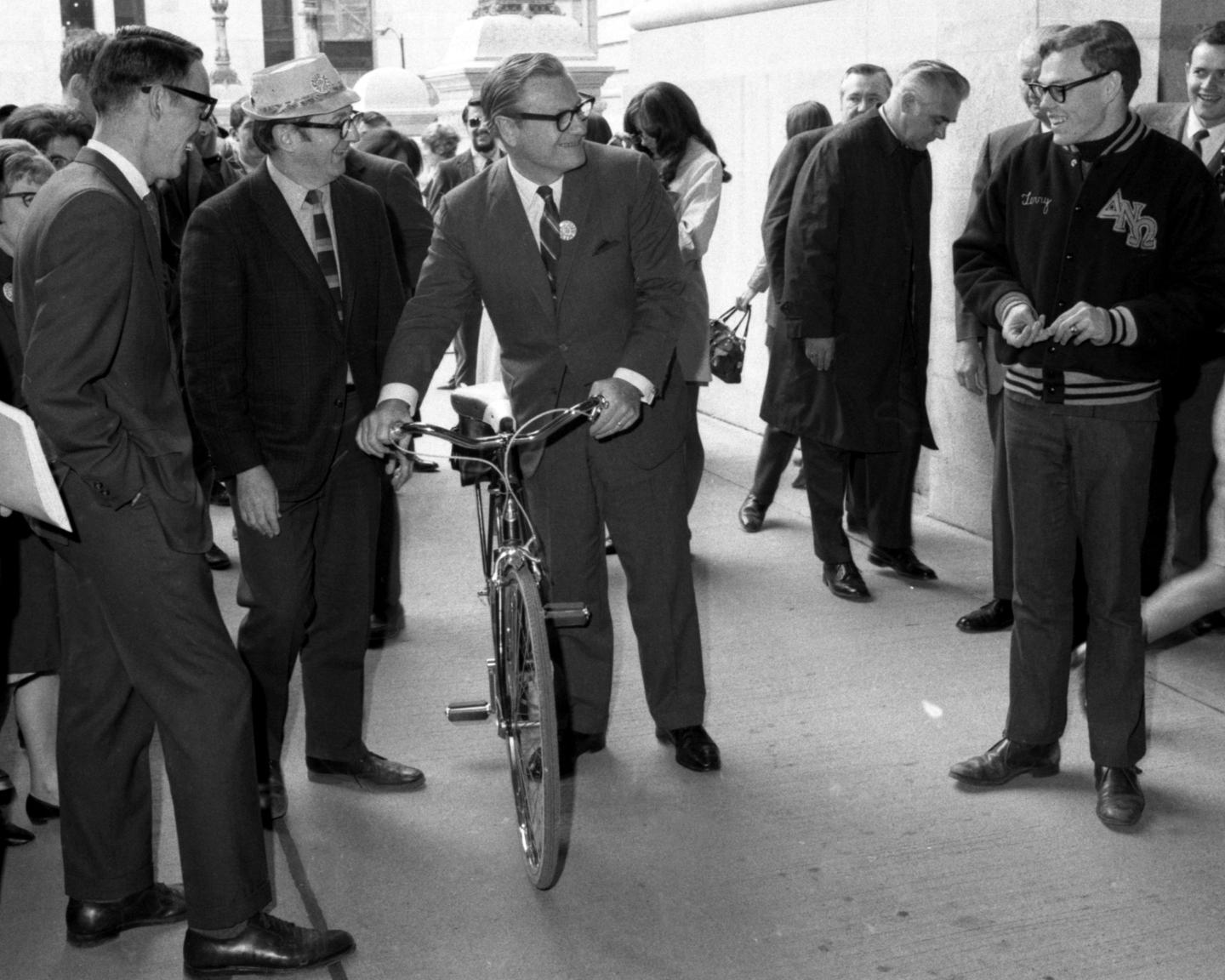 A businessman on a bicycle is surrounded by other businessmen.