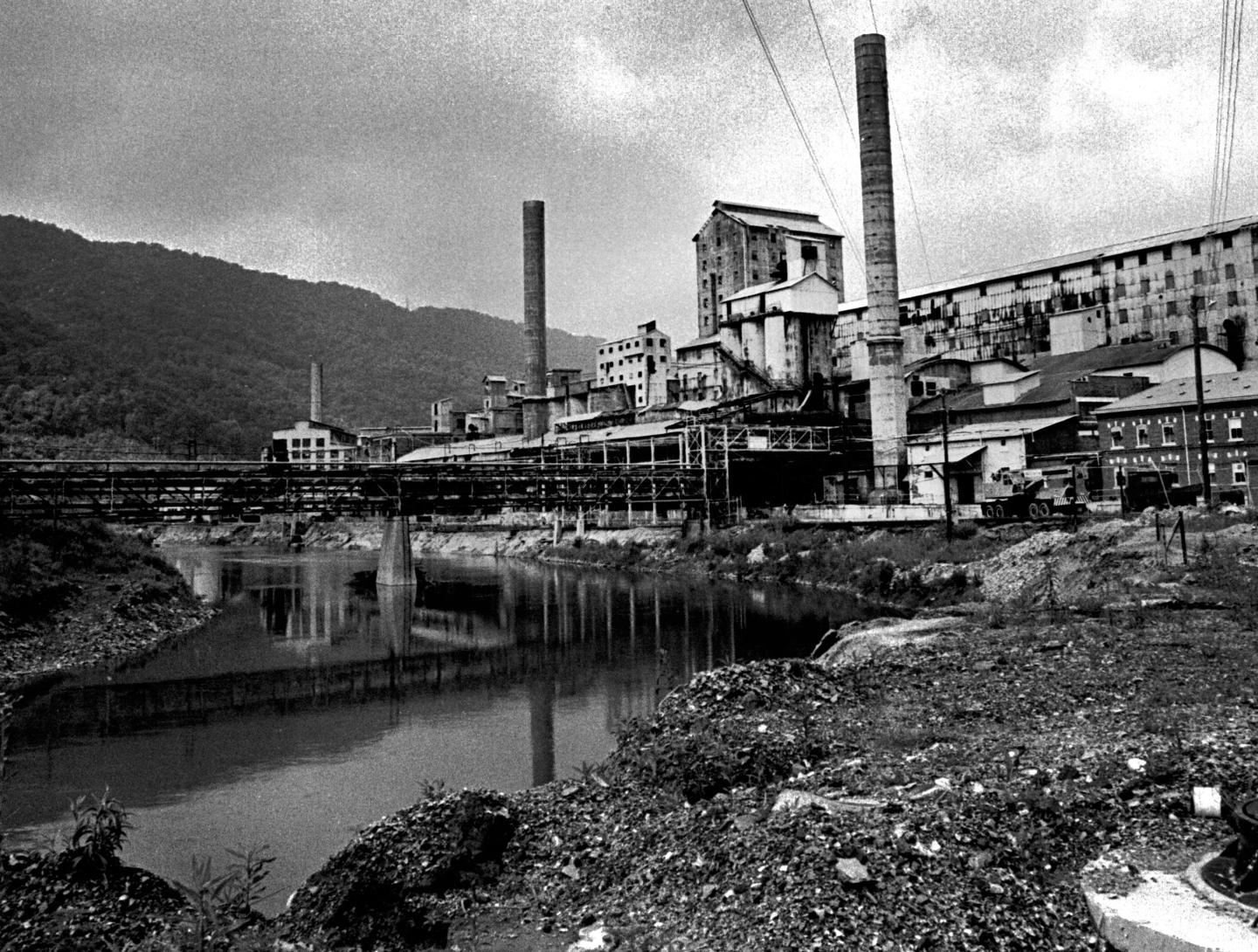 A black and white photo of an industrial factory next to a river.