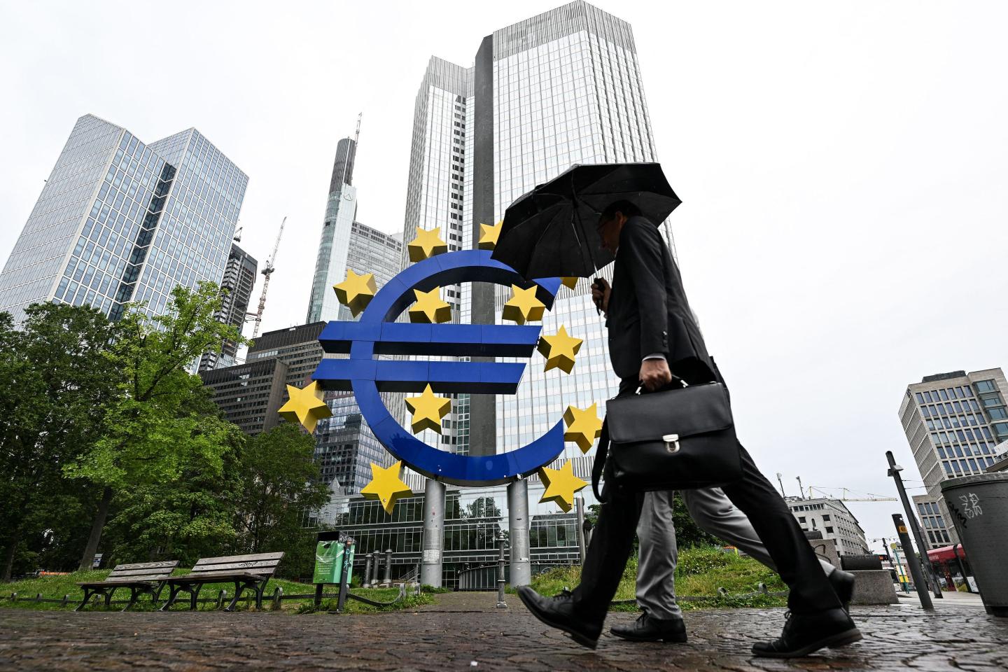 A man shelters from the rain under an umbrella as he walks past the Euro currency sign in front of the former European Central Bank (ECB) building in Frankfurt am Main, western Germany, on July 27, 2023 ahead of thr ECB's monthly announcement on eurozone monetary policy.