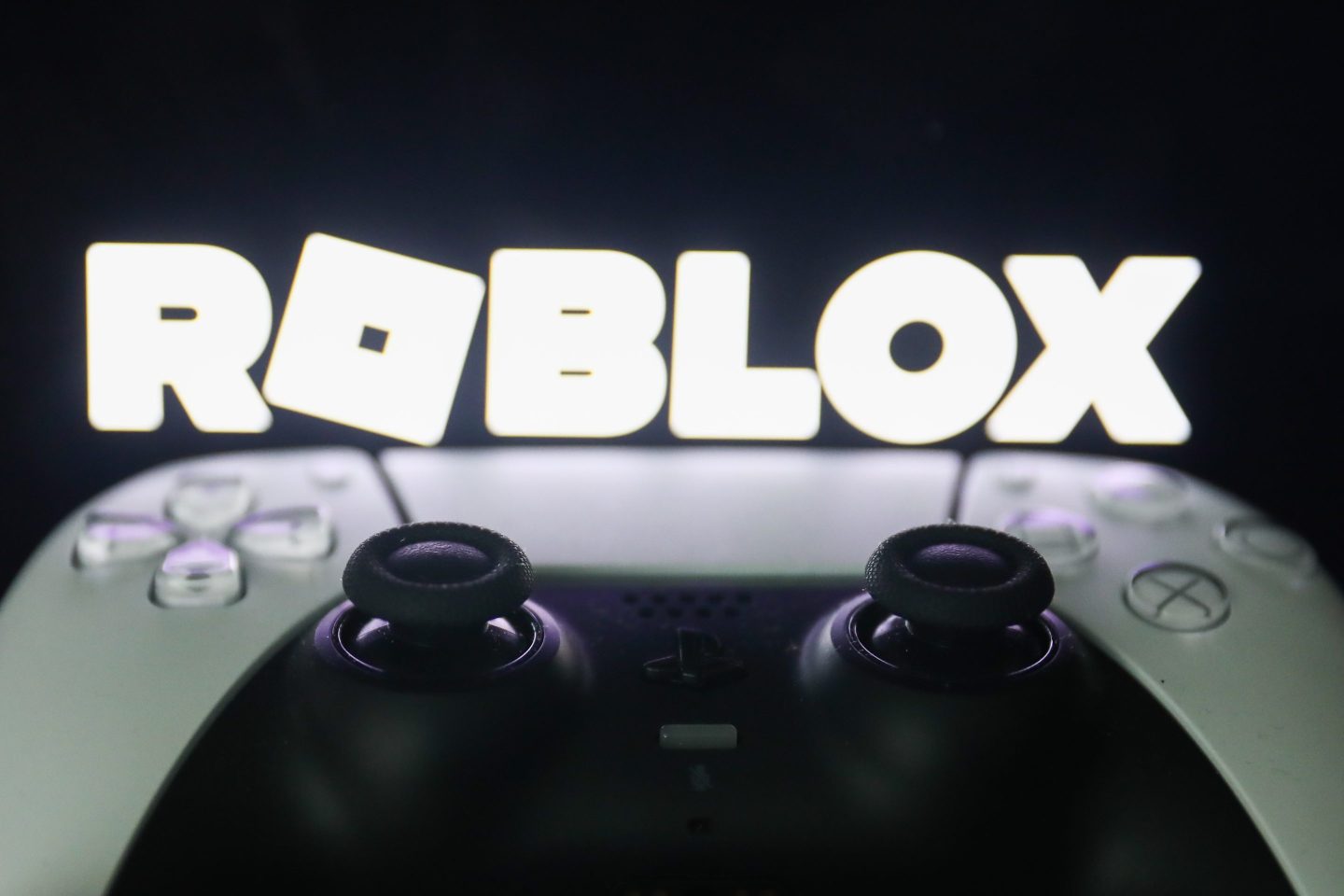 Roblox logo displayed on a screen and PlayStation DualSense controller are seen in this illustration.