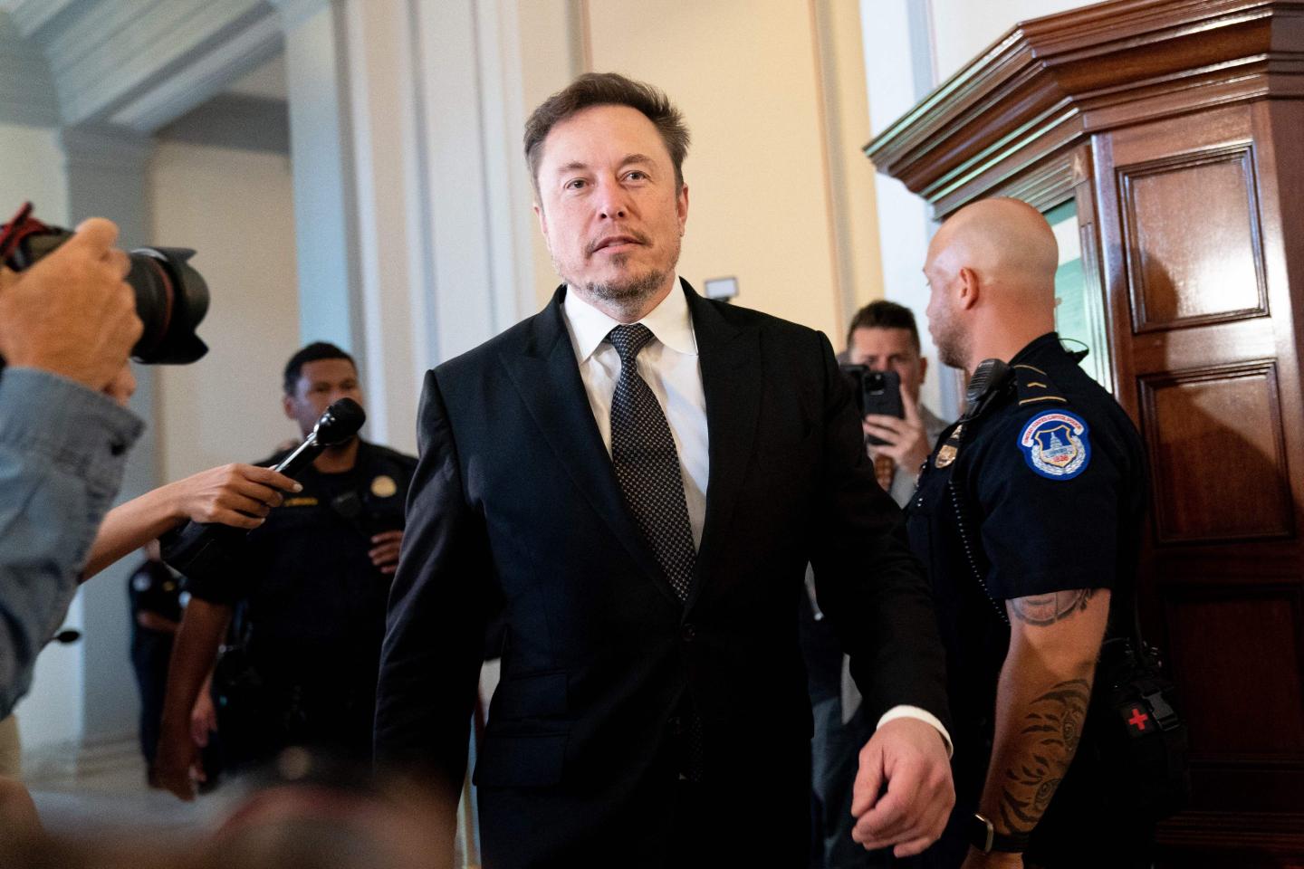 Elon Musk walking down a hallway in a suit