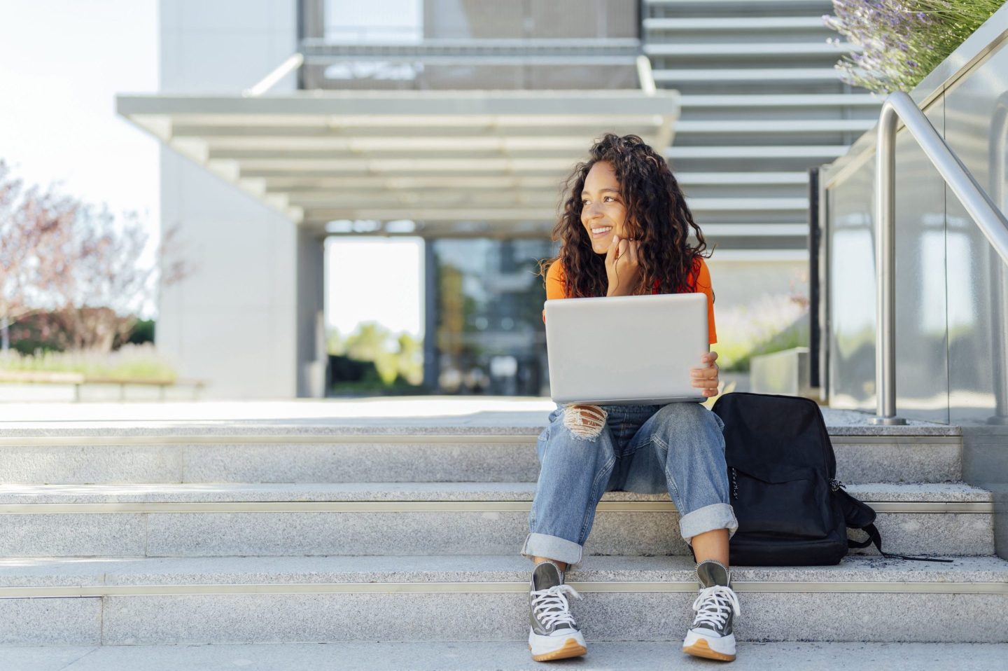 young person sits working on laptop on stairs outside