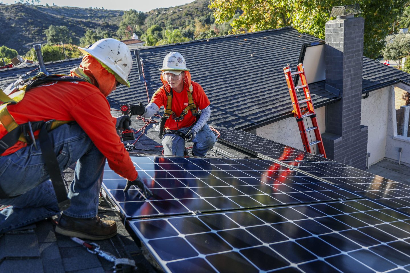 Workers install solar panels on the rooftop of a home in Poway, California.