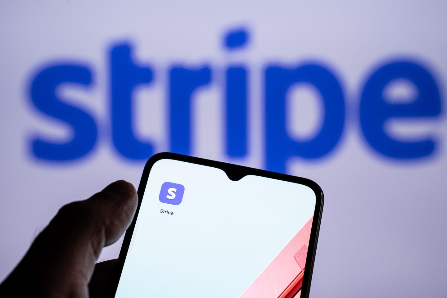 Someone holds a phone with the Stripe app in front of a screen displaying the Stripe logo