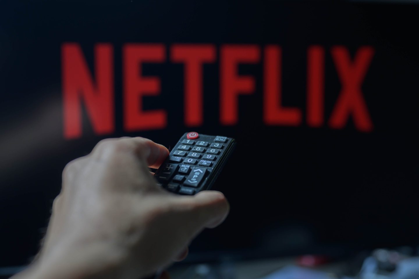 A person is holding a TV remote with Netflix visible in the background.