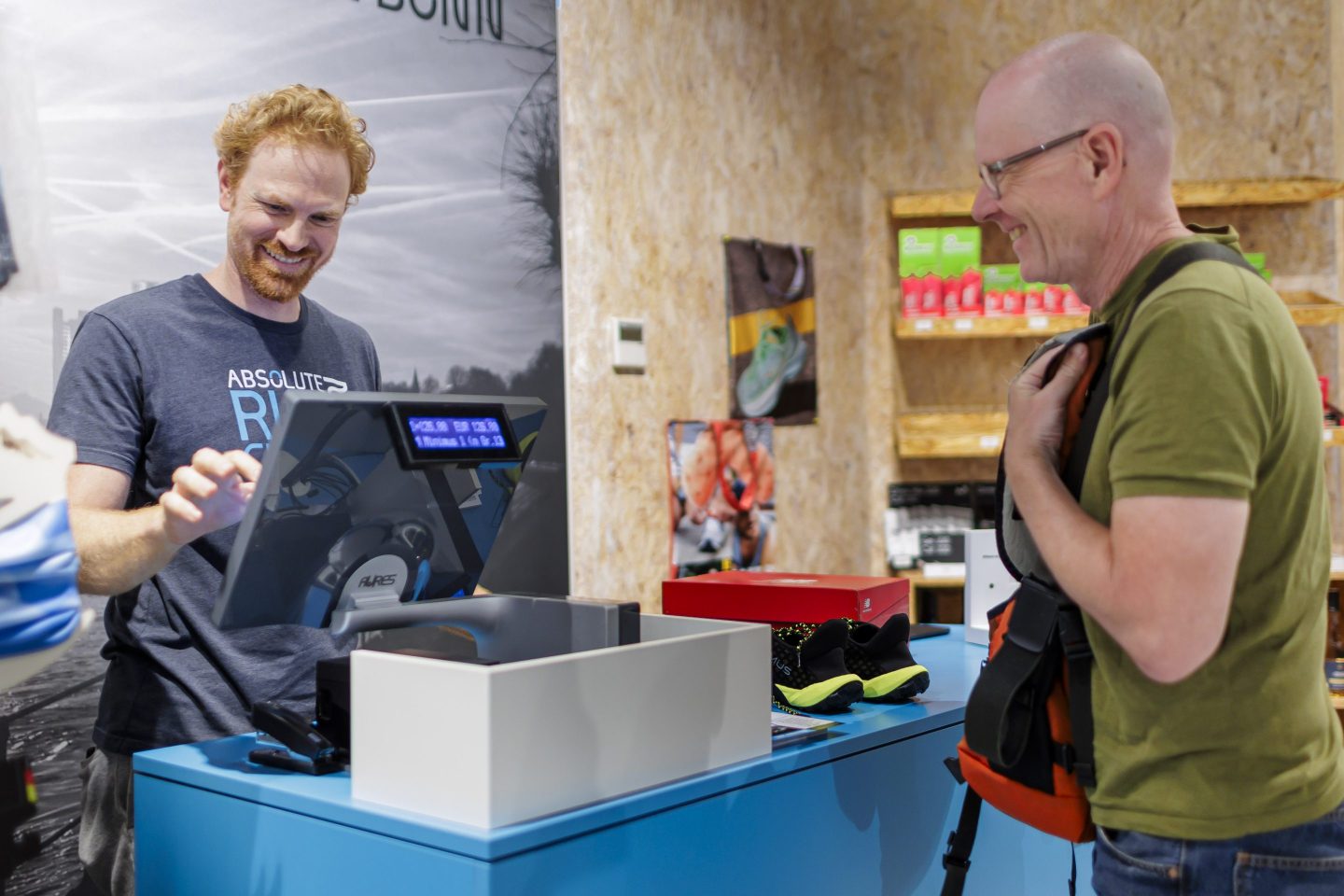 A man smiles to another man behind the register as he buys a pair of shoes.