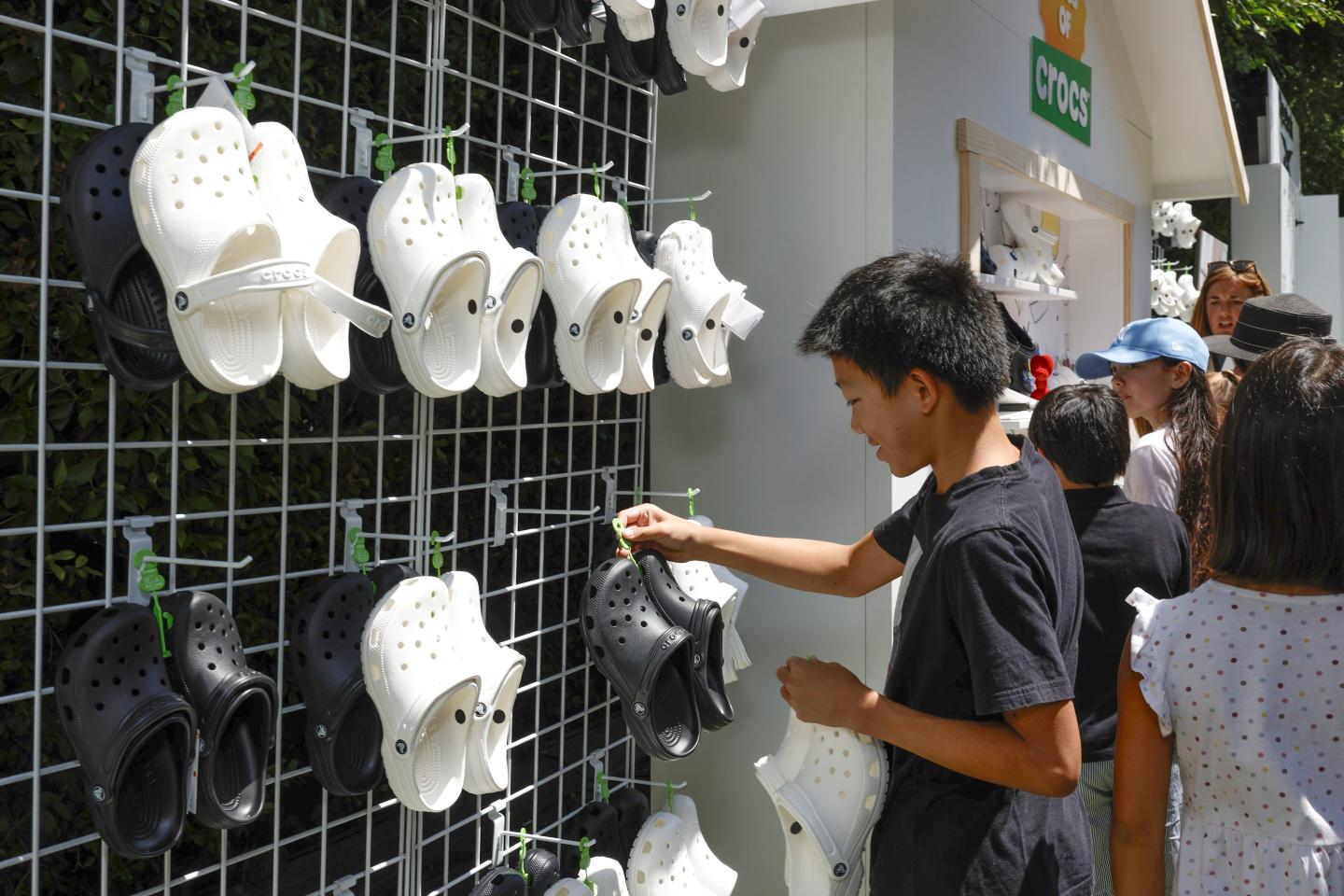 A kid picks a pair of Crocs off a vertical display shelf.