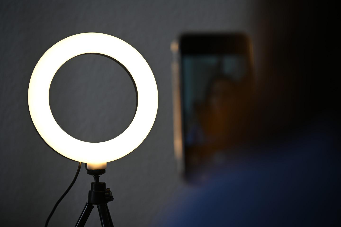 A woman sits behind a ring light and takes pictures of herself.