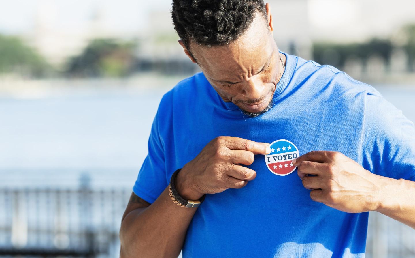 A mature man in his 40s putting an I VOTED sticker on his shirt.
