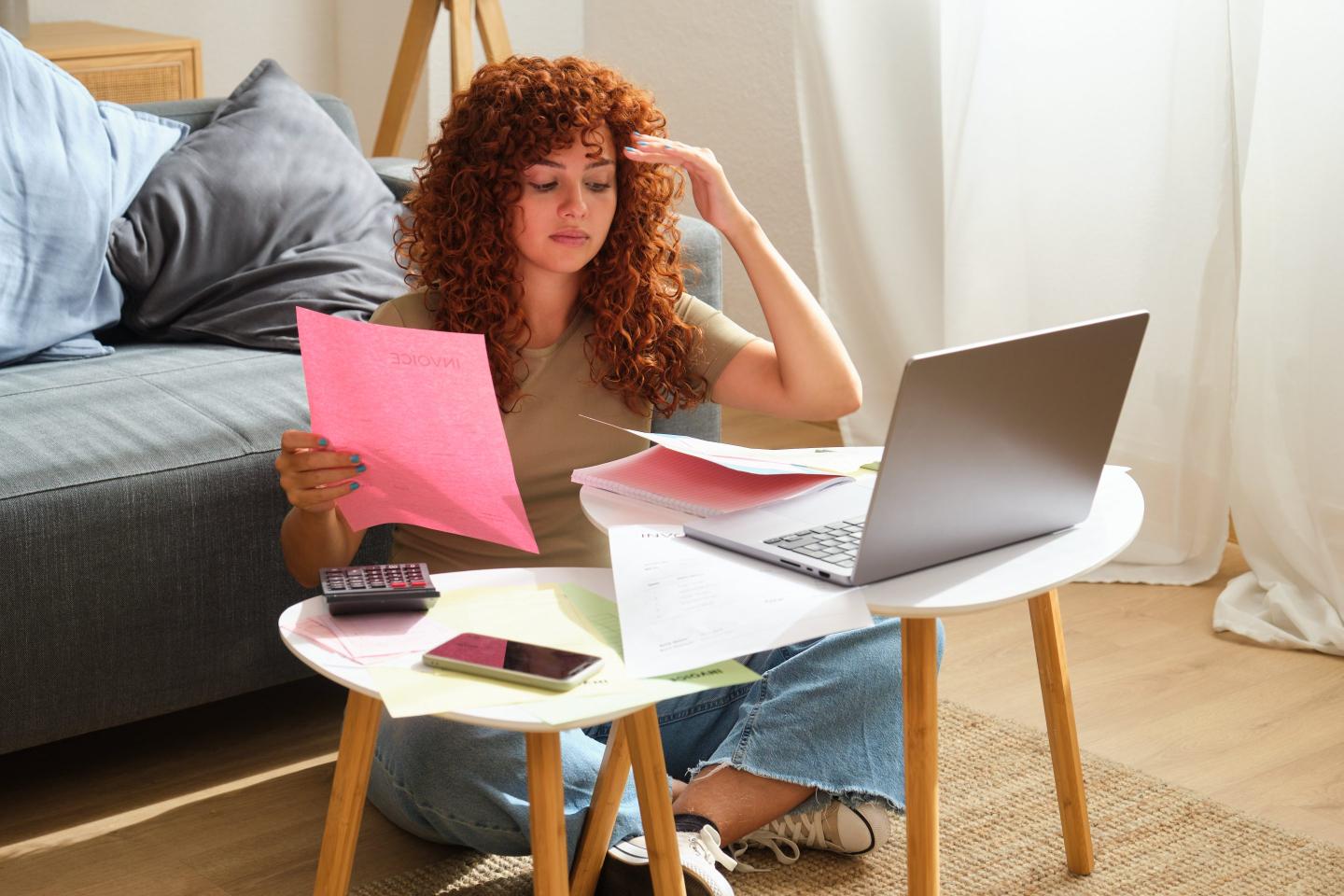 A woman with red hair sitting on the ground, working in front of a laptop