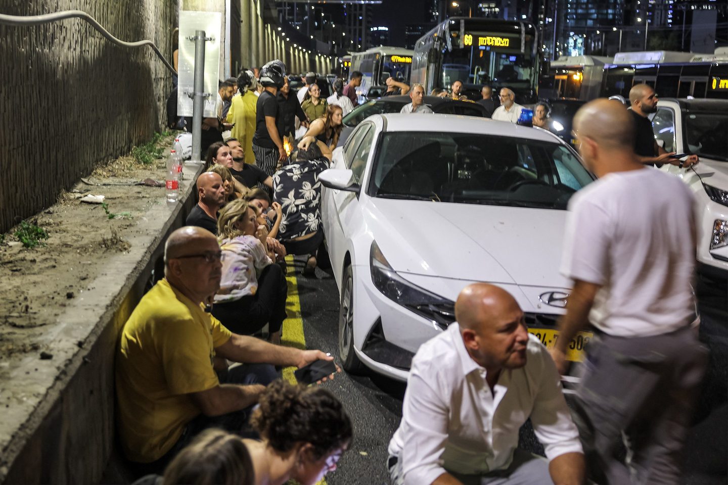 People take cover behind vehicles under a bridge along the side of a highway in Tel Aviv on Oct. 1, 2024.