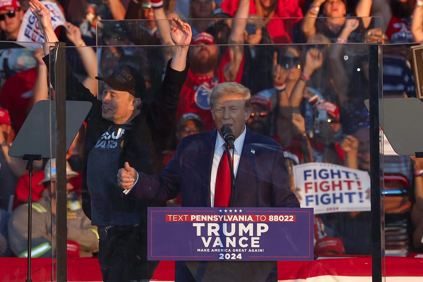 Elon Musk is seen cheering in the background of a Trump rally.