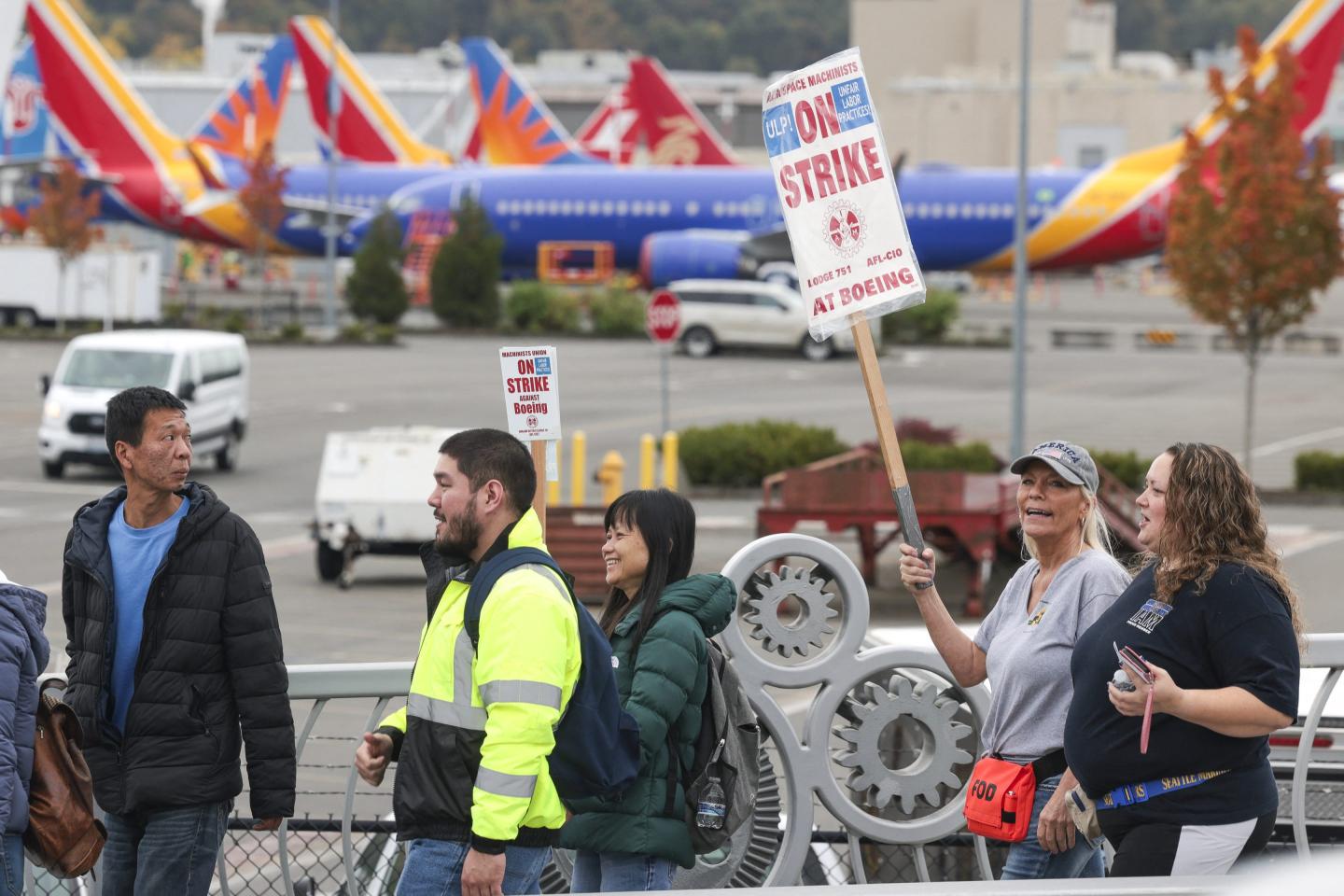 People carry Boeing-strike signs as they walk past parked Boeing 737 planes in the background.