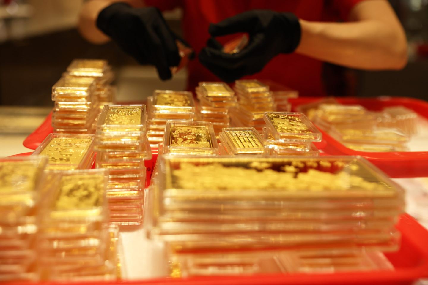 Hands are visible organizing trays of gold bars.