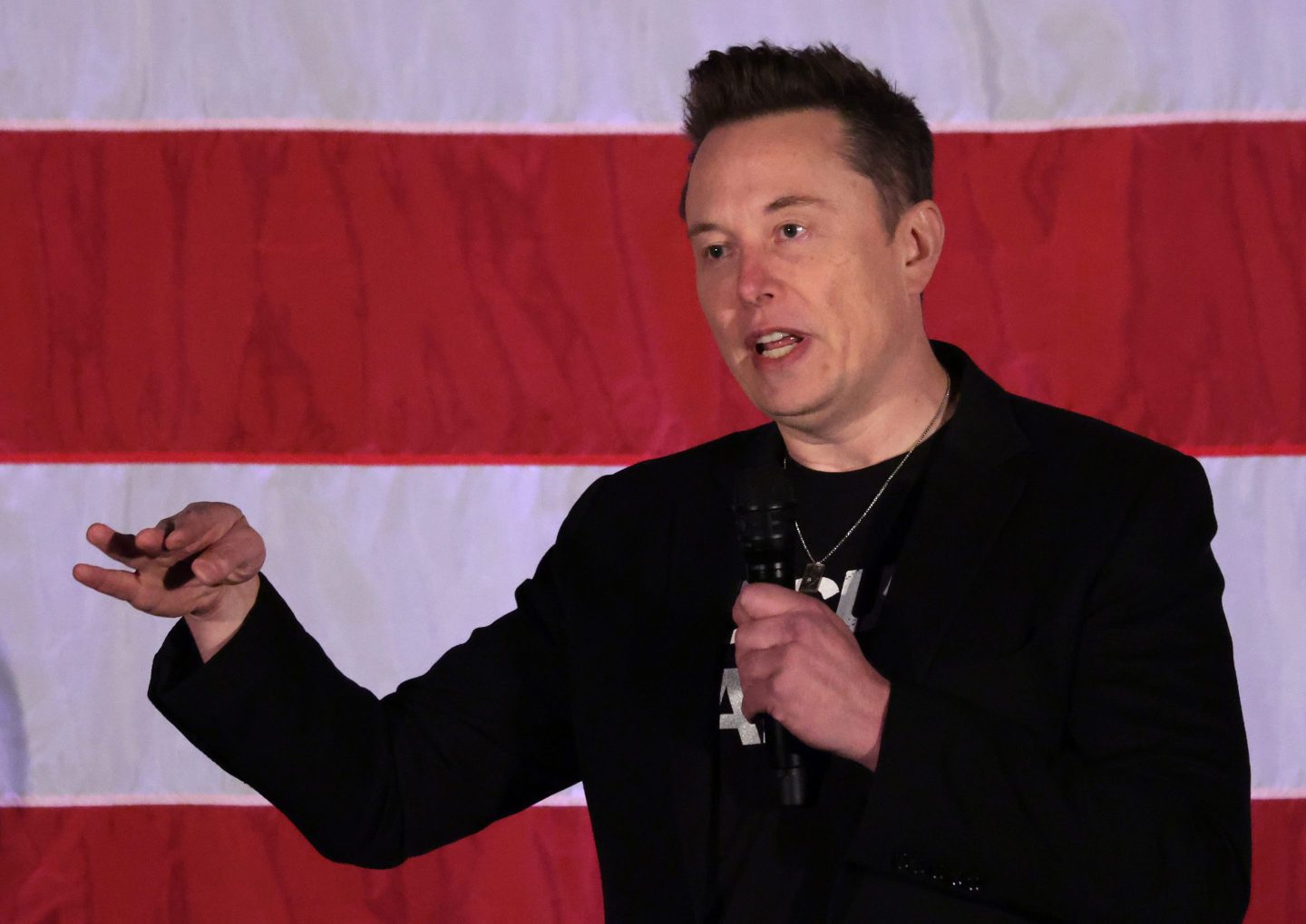 Tesla CEO Elon Musk talking on stage in front of an American flag