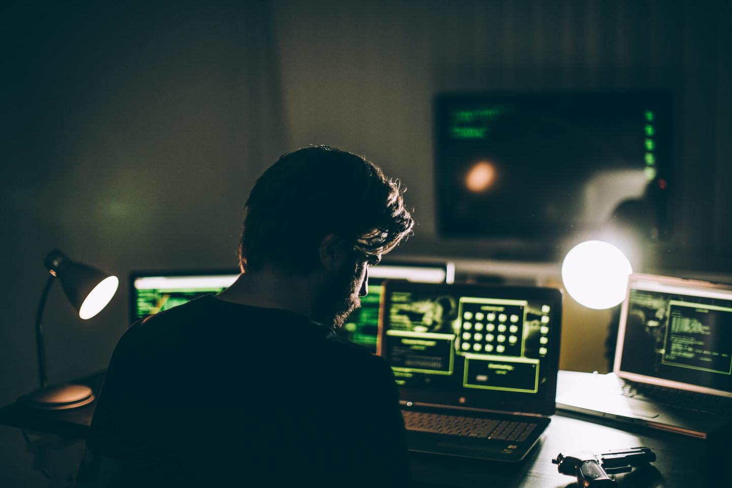 One man, sitting indoors surounded by computers, hacking crime is in motion, rear view.