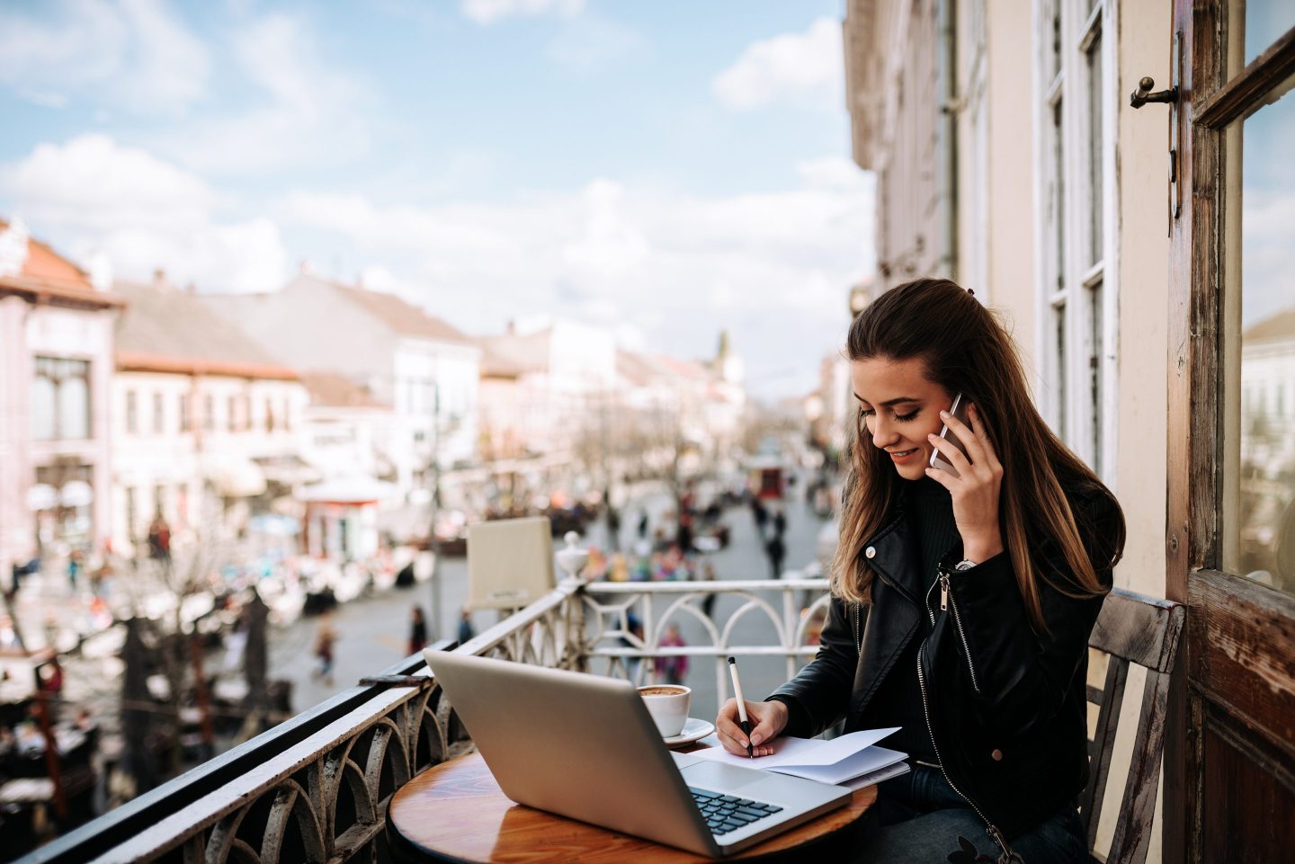 Young entrepreneur working outdoors at the cafe. Sitting on the balcony over the city street.