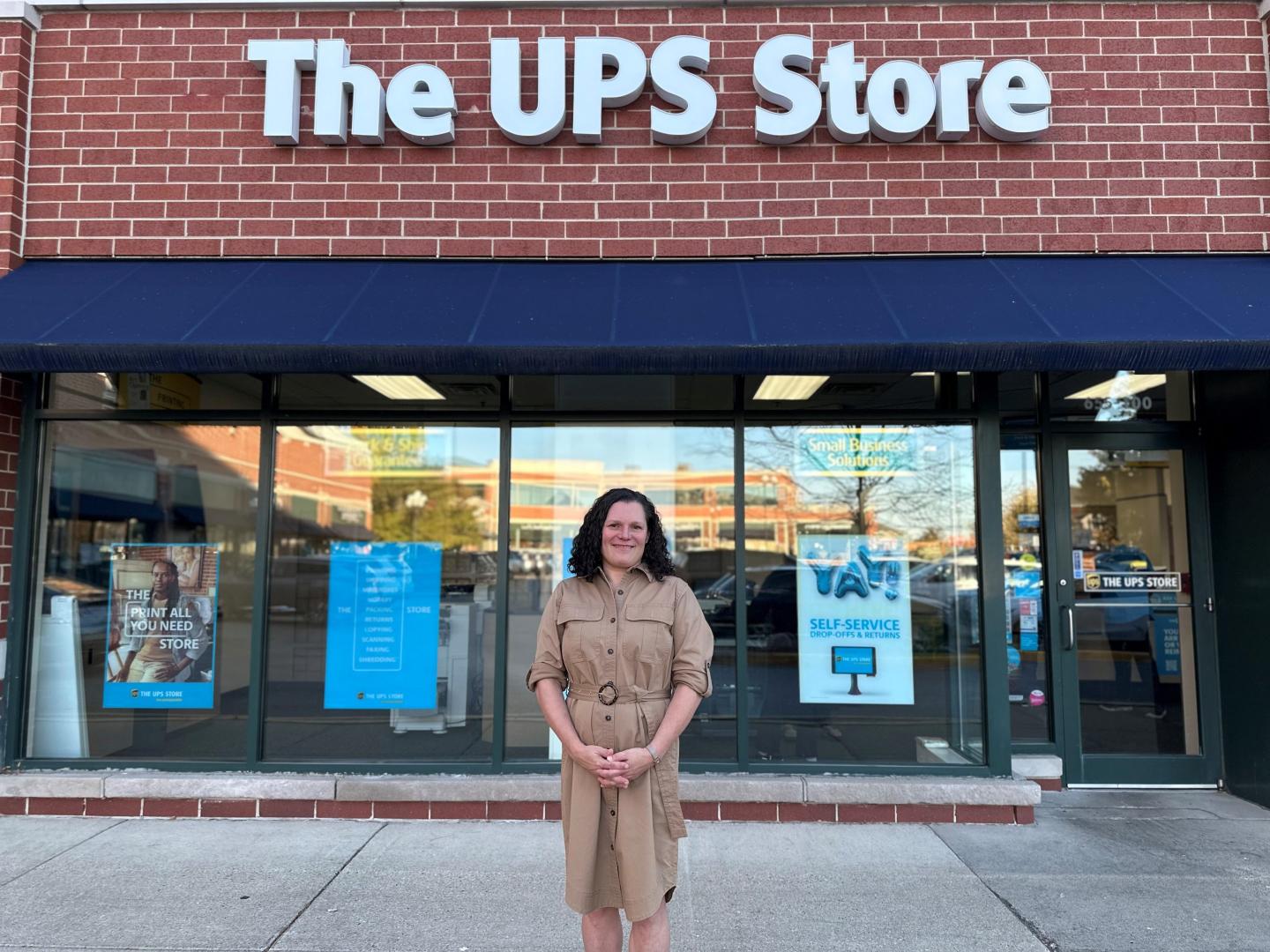 Woman in a tan shirt dress standing in front of a UPS Store