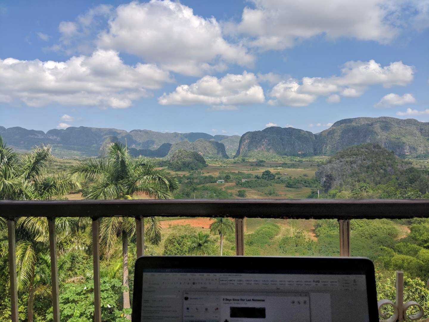 Photo of a laptop on a balcony overlooking rural hilltops