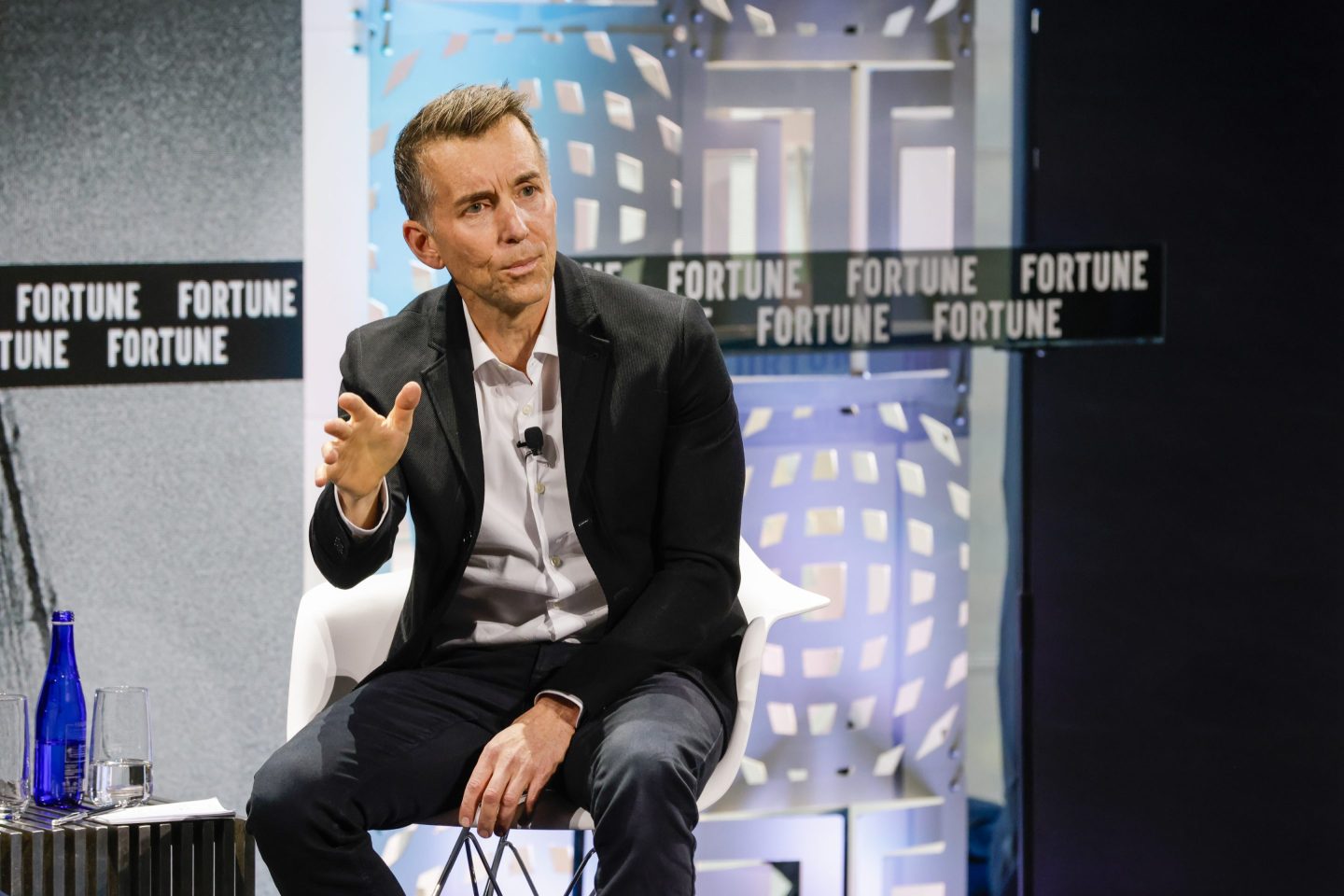 Zig Serafin looks away from camera with hand raised.