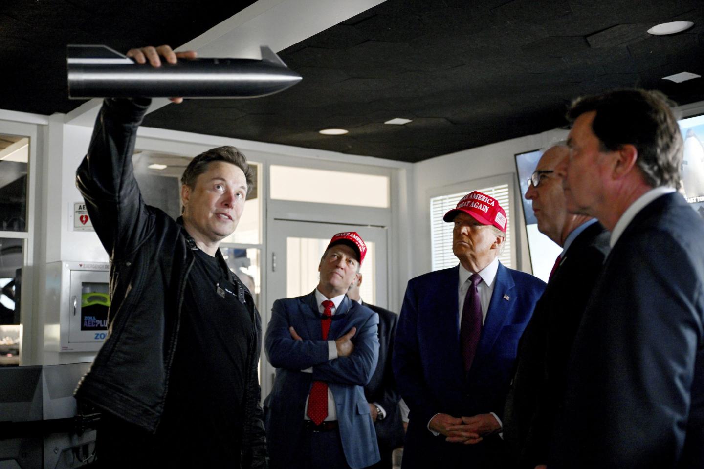 President-elect Donald Trump listens as Elon Musk holds a model rocket ship.