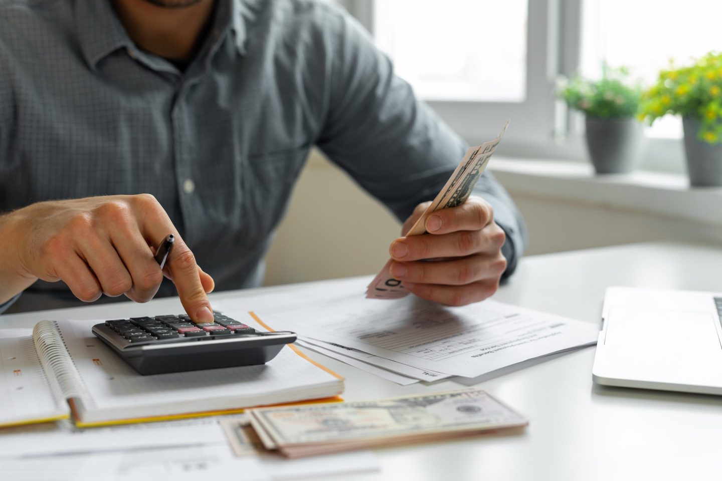 Man uses a calculator to count bills in his left hand.