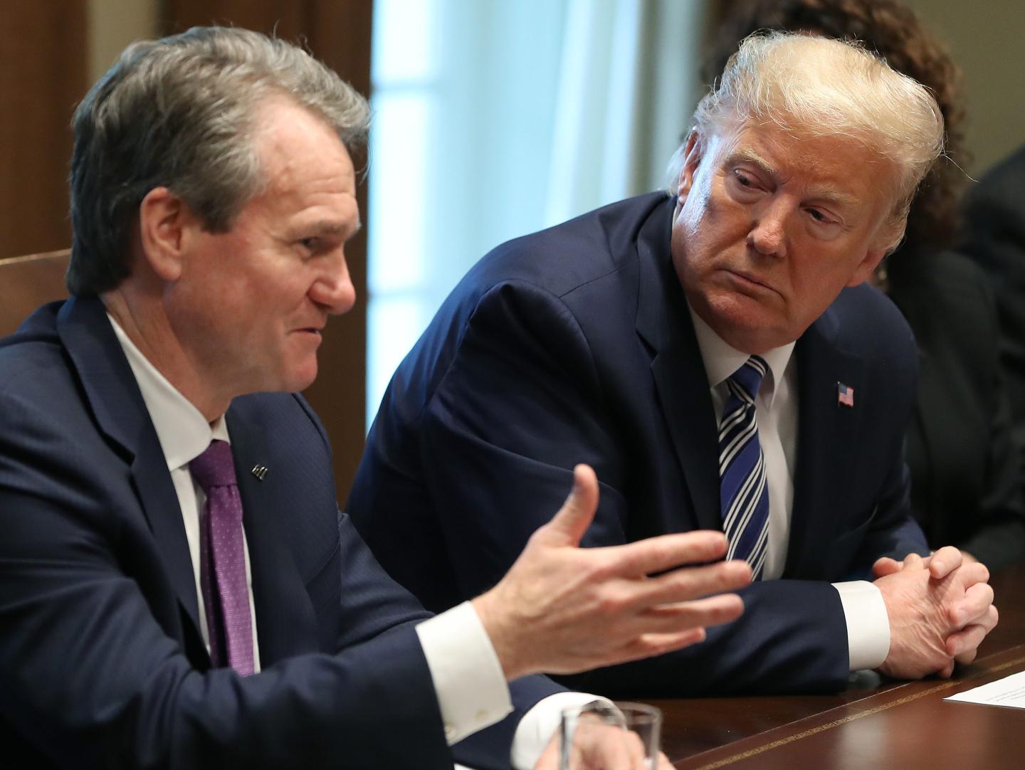 Donald Trump turns to his left and listens to Brian Moynihan, who raises his right hand as he speaks at a table.