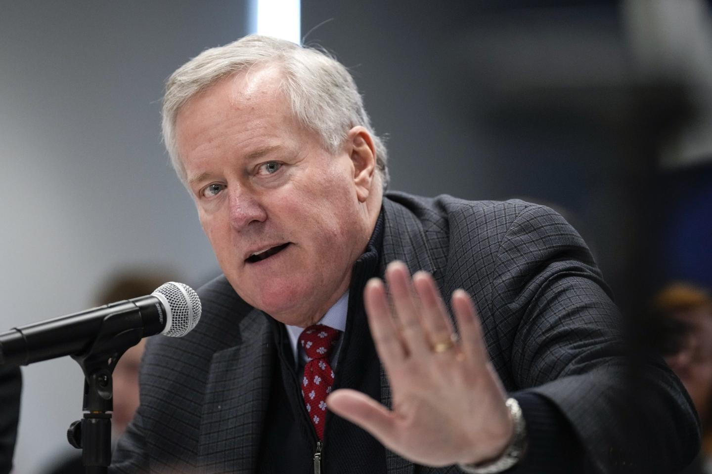 Mark Meadows sits in front of a microphone, holding up his hand