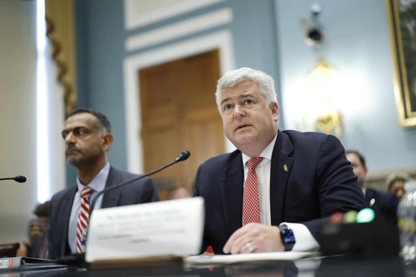 man in suit sitting in front of a microphone at a hearing