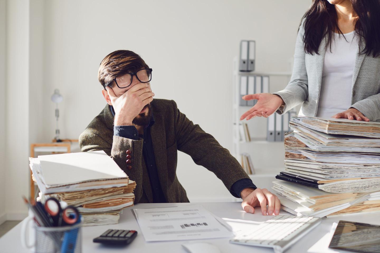 stressed worker at desk with stack of papers