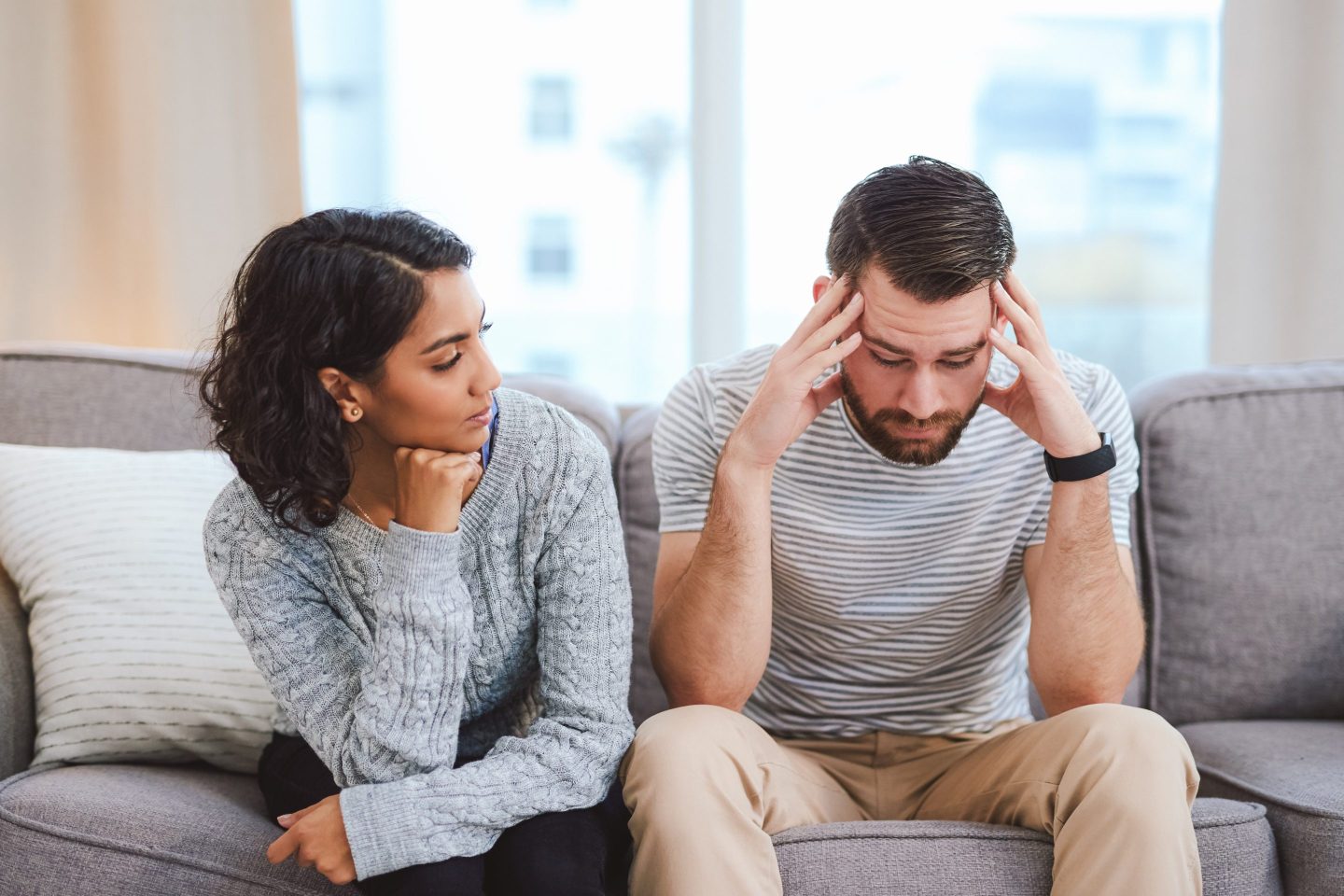 Woman and man sit together on a sofa, and he seems to be in distress