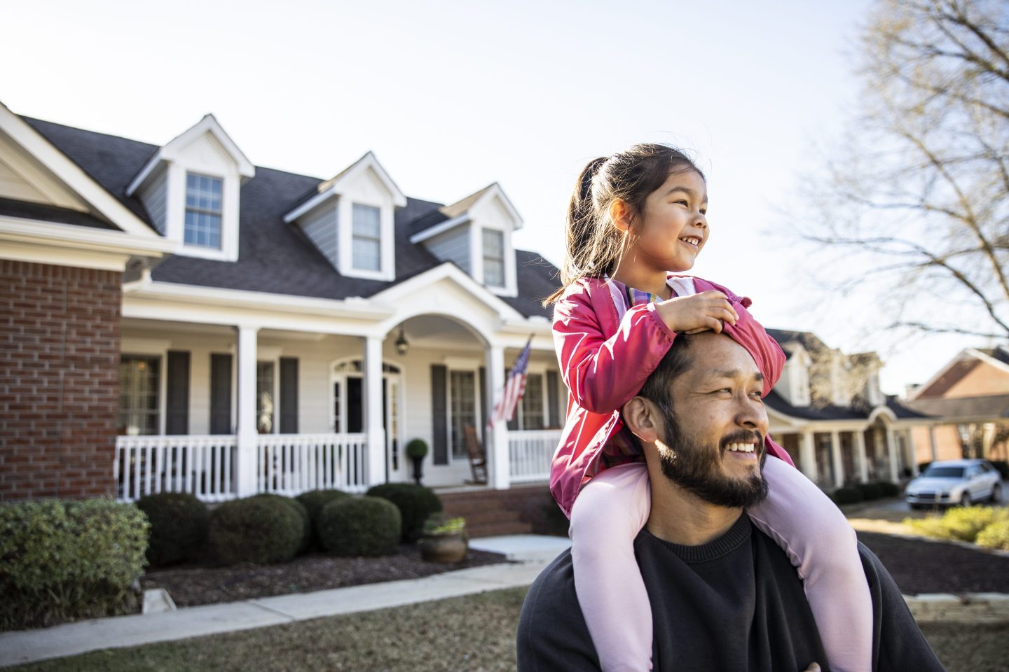 Daughter on father's shoulders in front of suburban home