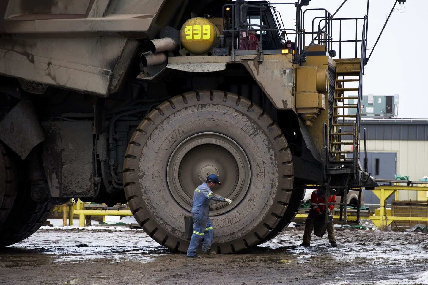 A worker on a mining site walks in front of the massive wheel of a mining vehicle.